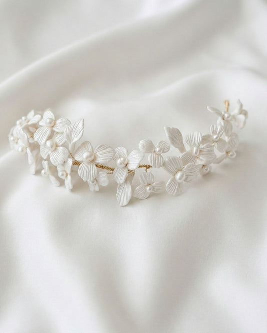 Tiara de novia modelo Alba hecha a mano con flores de porcelana fría blanca y centros de perlas sobre fondo de tela satinada. Accesorio nupcial artesanal de Pedra México.