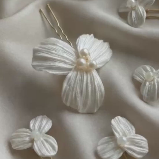 Video detallado del set de 5 horquillas Dalia para novia, mostrando la textura artesanal de los pétalos de porcelana fría y el brillo de las perlas centrales sobre tela satinada.