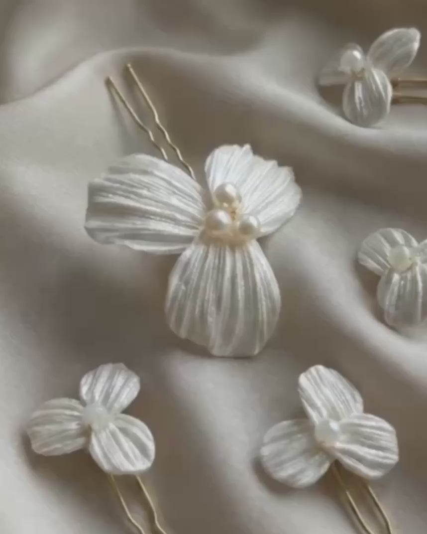 Video detallado del set de 5 horquillas Dalia para novia, mostrando la textura artesanal de los pétalos de porcelana fría y el brillo de las perlas centrales sobre tela satinada.