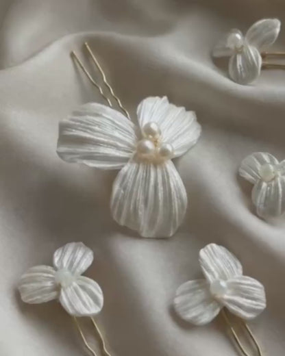 Video detallado del set de 5 horquillas Dalia para novia, mostrando la textura artesanal de los pétalos de porcelana fría y el brillo de las perlas centrales sobre tela satinada.