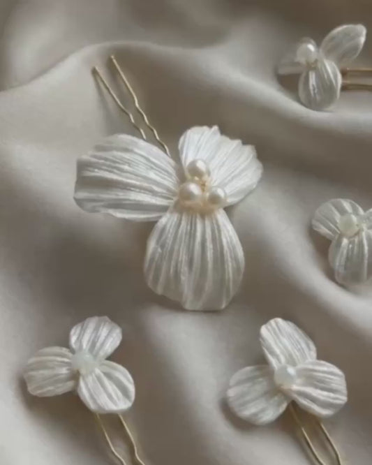 Video detallado del set de 5 horquillas Dalia para novia, mostrando la textura artesanal de los pétalos de porcelana fría y el brillo de las perlas centrales sobre tela satinada.