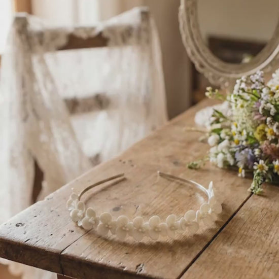 Video con zoom out que revela una diadema de flores de porcelana fría artesanal sobre una mesa de madera rústica, rodeada de elementos de boda vintage y flores naturales.
