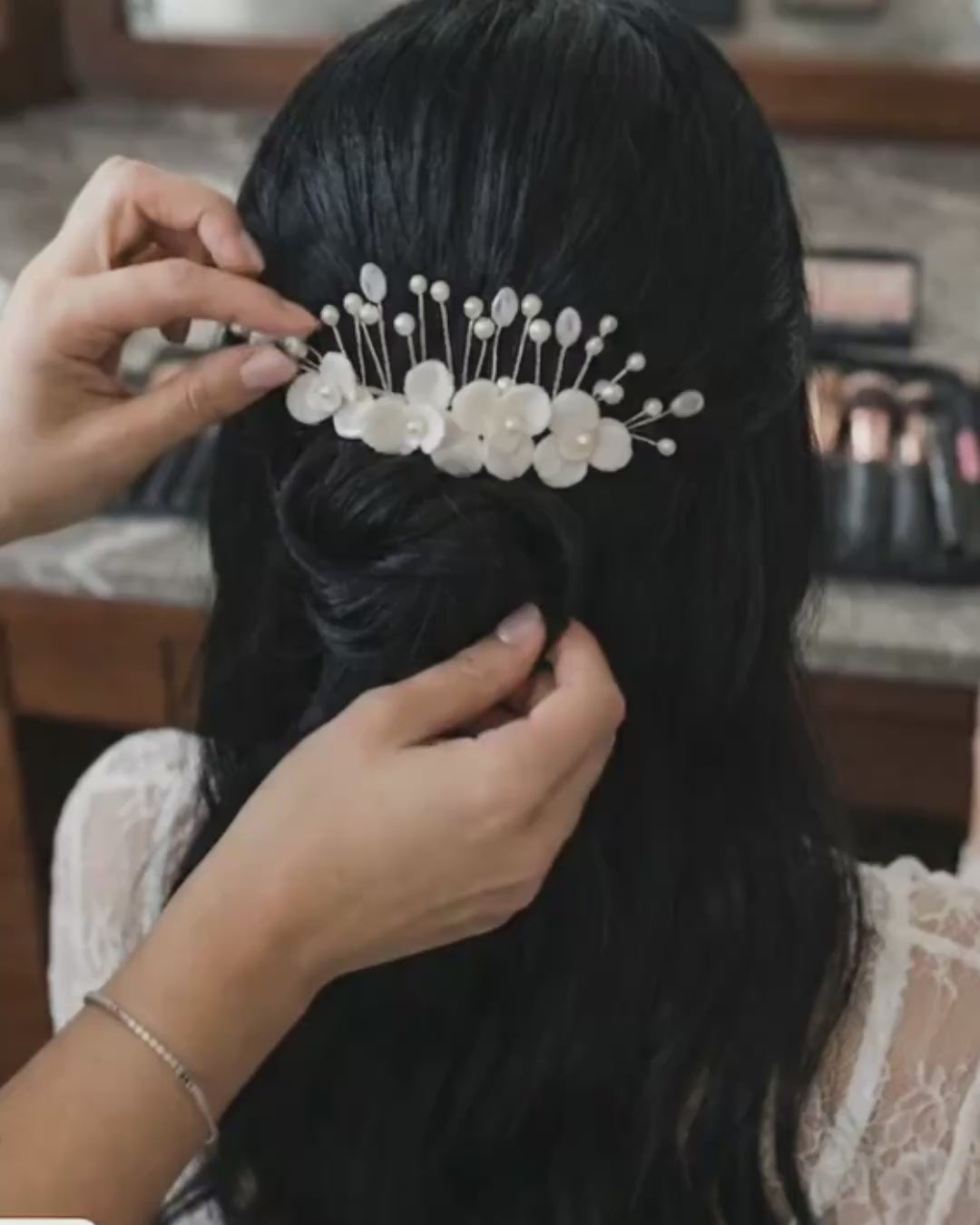 Primer plano de un tocado para novia Pedra hecho a mano con flores de porcelana marfil y detalles en perlas. Se muestra la textura y el acabado del accesorio siendo ajustado en un peinado de novia con cabello oscuro.