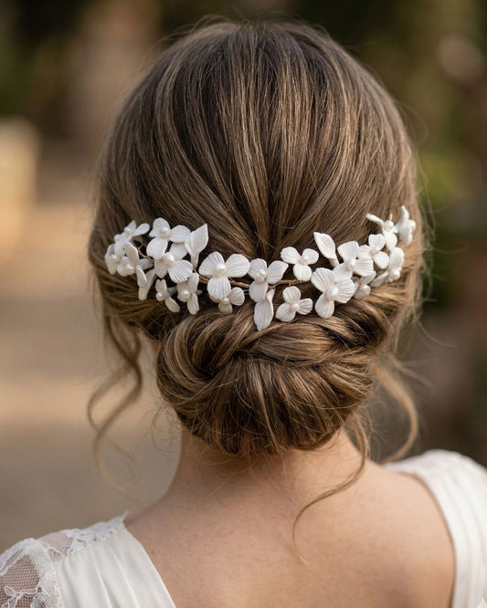 Tocado de novia artesanal en porcelana fría con flores blancas y perlas delicadas sobre un peinado recogido bajo texturizado. Joyería nupcial de Pedra México.